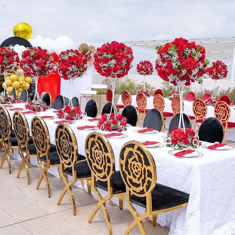 Beautiful wedding table with red and white floral arrangements and gold-accented chairs.